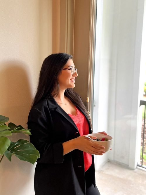 Vanessa holding a bowl of fruit by a window at home.